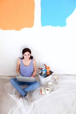 Yeni daire dizüstü bilgisayar ile oturup, boyama sırasında genç kadın portre. Dizüstü bilgisayar ile genç kadın