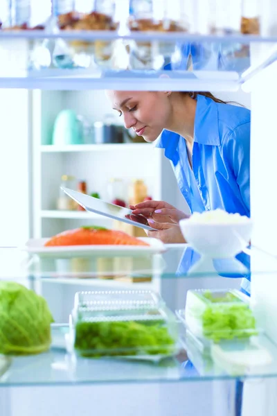 รูปภาพของผู้หญิงยืนอยู่ใกล้ตู้เย็นเปิดเต็มไปด้วยอาหารเพื่อสุขภาพผักและผลไม้ รูปภาพของผู้หญิง — ภาพถ่ายสต็อก