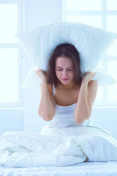 Joven mujer caucásica cubriendo su cabeza y orejas con almohadas — Foto de Stock