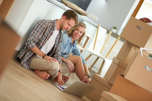 Young couple moving in new home.Sitting and relaxing after unpacking.Looking something on laptop. Young couple — Stock Photo, Image