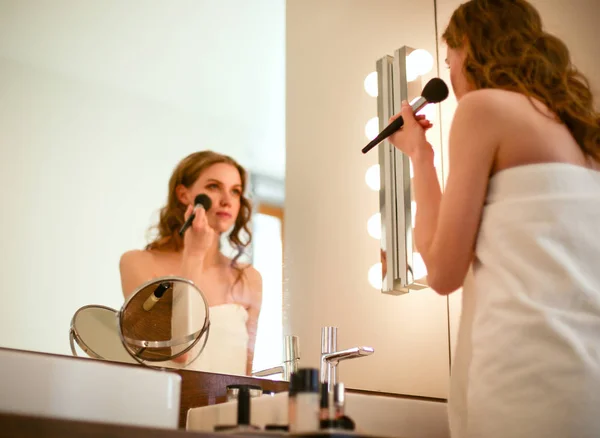 Young woman looking in the mirror and putting make-up on. — Stock Photo, Image