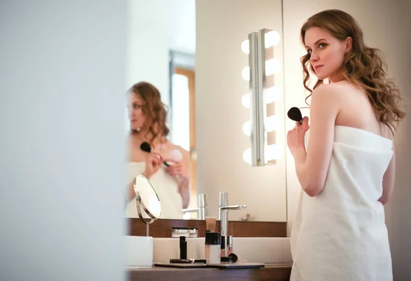 Ung kvinna tittar i spegeln och sätta smink på. — Stockfoto