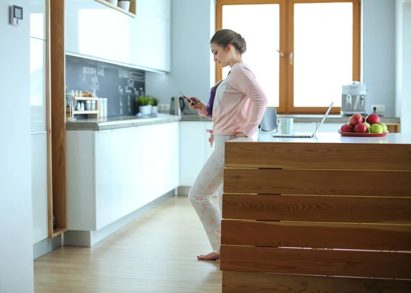 Mujer usando el teléfono móvil de pie en la cocina moderna . — Foto de Stock