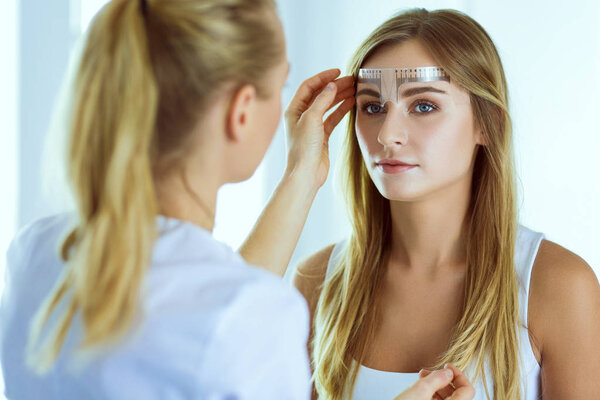 Permanent makeup for eyebrows. Closeup of beautiful woman with thick brows in beauty salon.