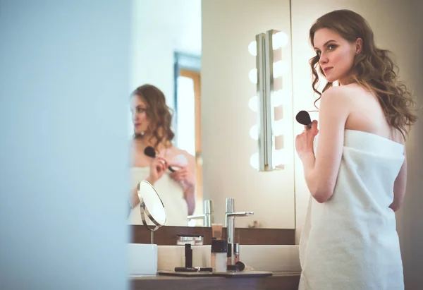 Молода жінка дивиться у дзеркало і одягає макіяж . — стокове фото