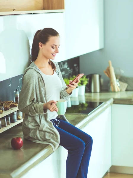 Mujer usando el teléfono móvil sentado en la cocina moderna . — Foto de Stock