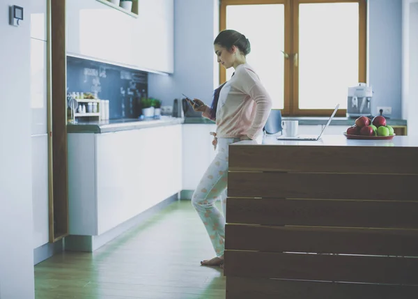 Mujer usando el teléfono móvil de pie en la cocina moderna . — Foto de Stock