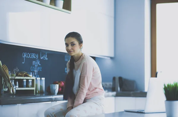 Young woman sitting on table in the kitchen. — Stock Photo, Image