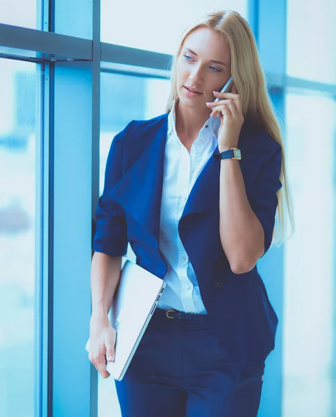 Бизнесмен, стоящая у окна офиса и разговаривающая по мобильному телефону. Бизнесвумен — стоковое фото