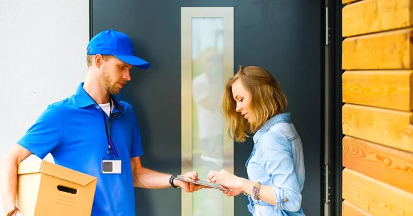 Repartidor sonriente con uniforme azul que entrega la caja de paquetes al destinatario: concepto de servicio de mensajería. Repartidor sonriente en uniforme azul — Foto de Stock