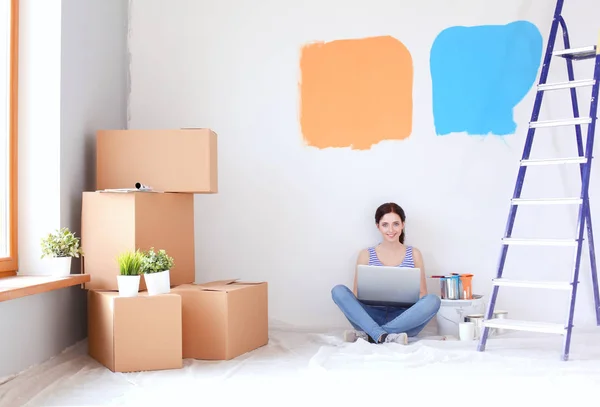Retrato de mujer joven mientras pinta nuevo apartamento, sentado con el ordenador portátil. Mujer joven con portátil — Foto de Stock