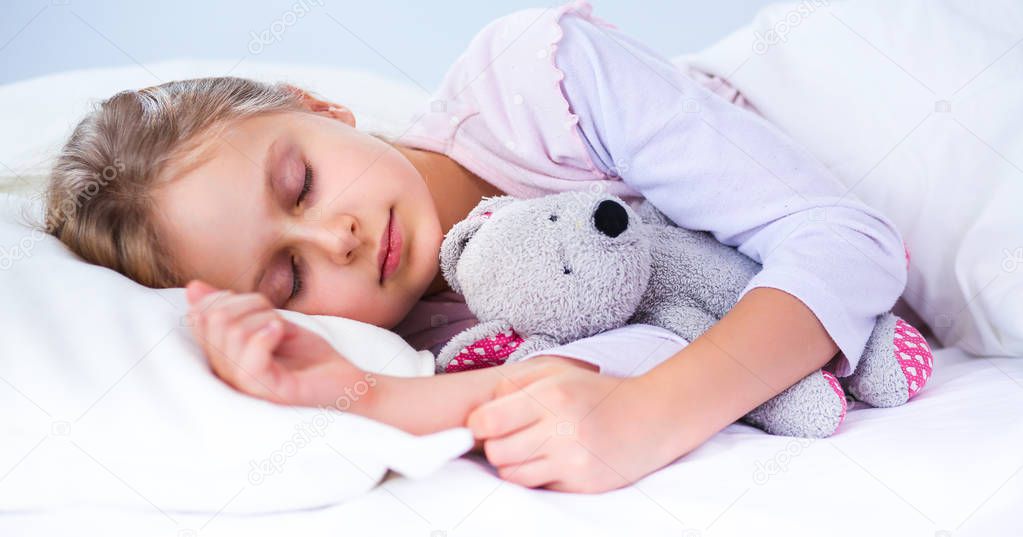 Child little girl sleeps in the bed with a toy teddy bear