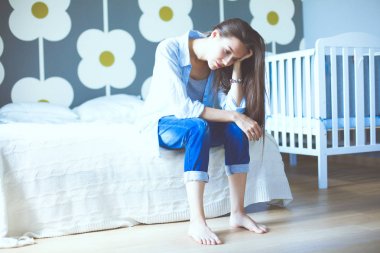 Genç çocuk karyolası yakın yatağın üstüne oturan kadın yorgun. Genç anne.