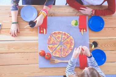 Ahşap masada otururken birlikte yemek yiyen bir grup insanın üst düzey görüntüsü. Masada yemek var. İnsanlar fast food yiyor..