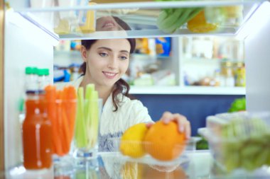 Sağlıklı yiyecek, sebze ve meyvelerle dolu açık buzdolabının yanında duran kadın portresi. Kadın portresi