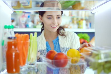 Sağlıklı yiyecek, sebze ve meyvelerle dolu açık buzdolabının yanında duran kadın portresi. Kadın portresi