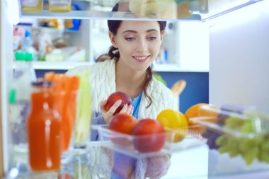 Sağlıklı yiyecek, sebze ve meyvelerle dolu açık buzdolabının yanında duran kadın portresi. Kadın portresi