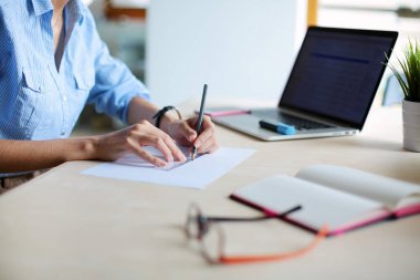 Ofis masasında dizüstü bilgisayarla oturan genç bir kadın. Genç bir kadın. Dizüstü bilgisayar