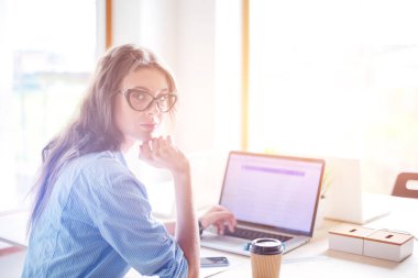 Ofis masasında oturan genç bir kadın dizüstü bilgisayar ekranına bakıyor. Genç kadın.