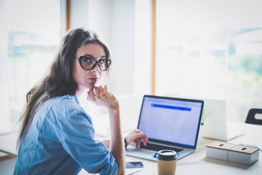 Ofis masasında oturan genç bir kadın dizüstü bilgisayar ekranına bakıyor. Genç kadın.