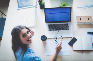 Ofis masasında oturan genç bir kadın dizüstü bilgisayar ekranına bakıyor. Genç kadın.