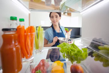 Sağlıklı yiyecek, sebze ve meyvelerle dolu açık buzdolabının yanında duran kadın portresi. Kadın portresi