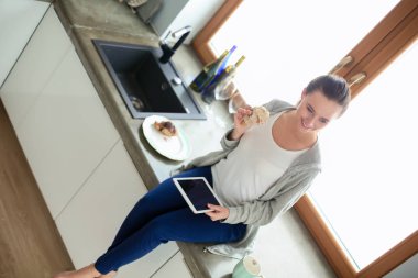 Mutfakta dijital tablet kullanan güzel genç bir kadın..