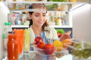 Sağlıklı yiyecek, sebze ve meyvelerle dolu açık buzdolabının yanında duran kadın portresi. Kadın portresi