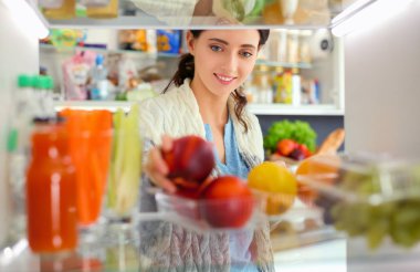 Sağlıklı yiyecek, sebze ve meyvelerle dolu açık buzdolabının yanında duran kadın portresi. Kadın portresi