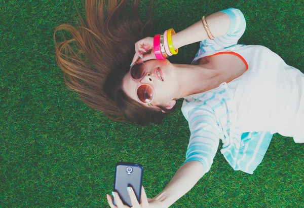 Mooie jonge vrouw die selfie maakt door haar telefoon terwijl ze in groen gras ligt. mooie jonge vrouw maken selfie — Stockfoto