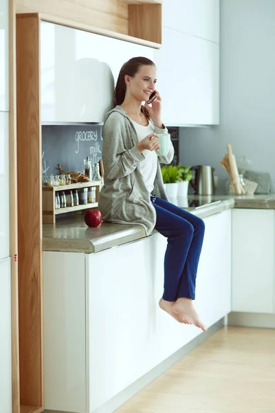 Женщина с помощью мобильного телефона сидит на современной кухне . — стоковое фото