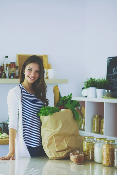 Jeune femme tenant sac d'épicerie avec des légumes. Debout dans la cuisine. Jeune femme — Photo