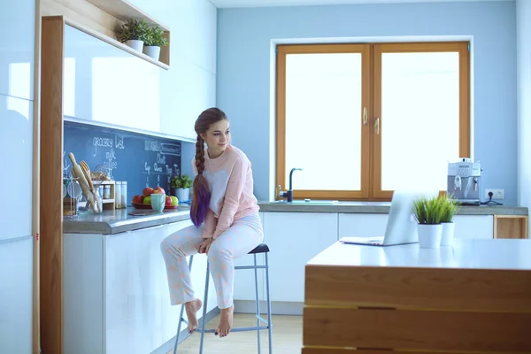 Молодая женщина сидит на столе на кухне . — стоковое фото