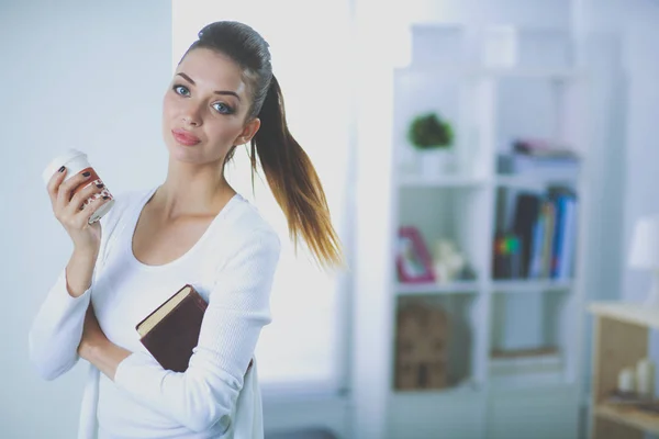Attraktive Geschäftsfrau steht mit Buch an Wand im Büro. — Stockfoto