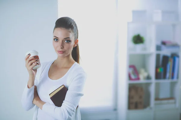 Attractive businesswoman standing near wall in office with book. — Stock Photo, Image