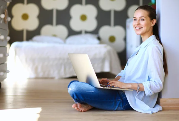 Ung kvinna som sitter på golvet nära barnens babysäng med laptop. Ung mamma — Stockfoto