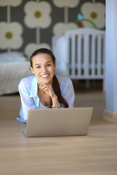 年轻的女人坐在笔记本电脑的儿童床边的地板上。年轻的妈妈 — 图库照片