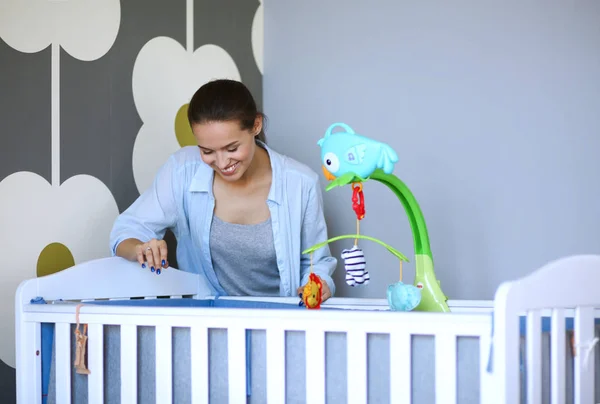 Ung kvinna som står nära barnens spjälsäng. Ung mamma — Stockfoto