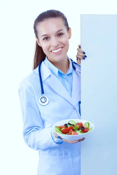 Портрет красивої жінки-лікаря, який тримає тарілку зі свіжими овочами, що стоять поруч з порожньою. Жінка лікарі — стокове фото