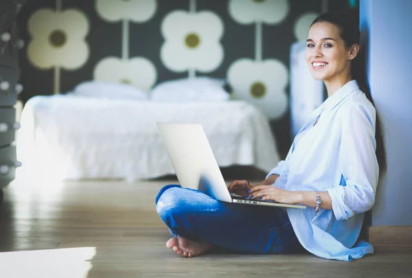 Ung kvinna som sitter på golvet nära barnens babysäng med laptop. Ung mamma — Stockfoto