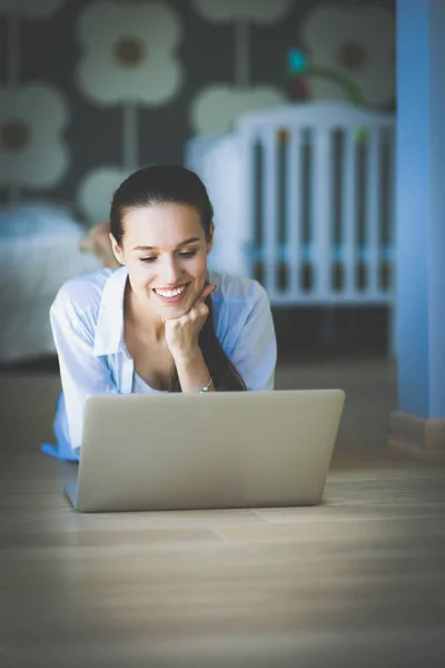 Giovane donna seduta sul pavimento vicino a lettino per bambini con computer portatile. Giovane mamma — Foto Stock