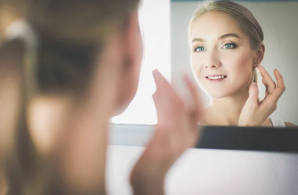 Жінка піклується про її красиву шкіру на обличчі, що стоїть біля дзеркала — стокове фото