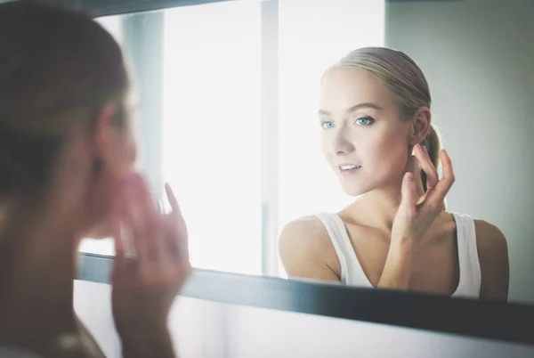 Frau pflegt ihre schöne Haut im Gesicht, die neben dem Spiegel steht — Stockfoto