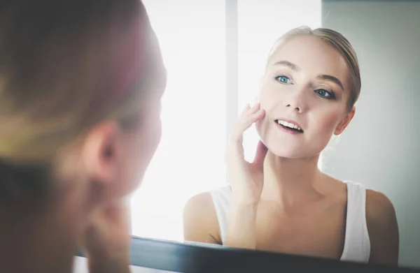 Wanita merawat kulitnya yang indah di wajah berdiri di dekat cermin — Stok Foto