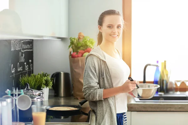 Ung kvinna förbereder pannkakor i köket när du står nära bordet. Kvinnan i köket. Matlagning i köket. — Stockfoto