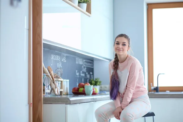 Jovem mulher sentada na mesa na cozinha . — Fotografia de Stock