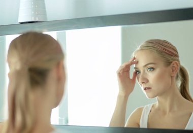 Genç ve sağlıklı bir kadının yüzü ve aynadaki yansıması.