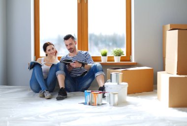 Yeni evin içini boyayan mutlu, gülümseyen genç bir çift portresi. Genç çift