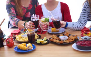 Ahşap masada otururken birlikte yemek yiyen bir grup insanın üst düzey görüntüsü. Masada yemek var. İnsanlar fast food yiyor..