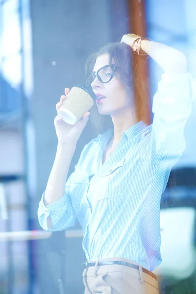 Mujer joven sentada en la mesa de la oficina con portátil, vista a través de la ventana. Mujer joven —  Fotos de Stock